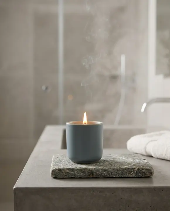 Bougie Source allumée sur une pierre au bord d’une baignoire